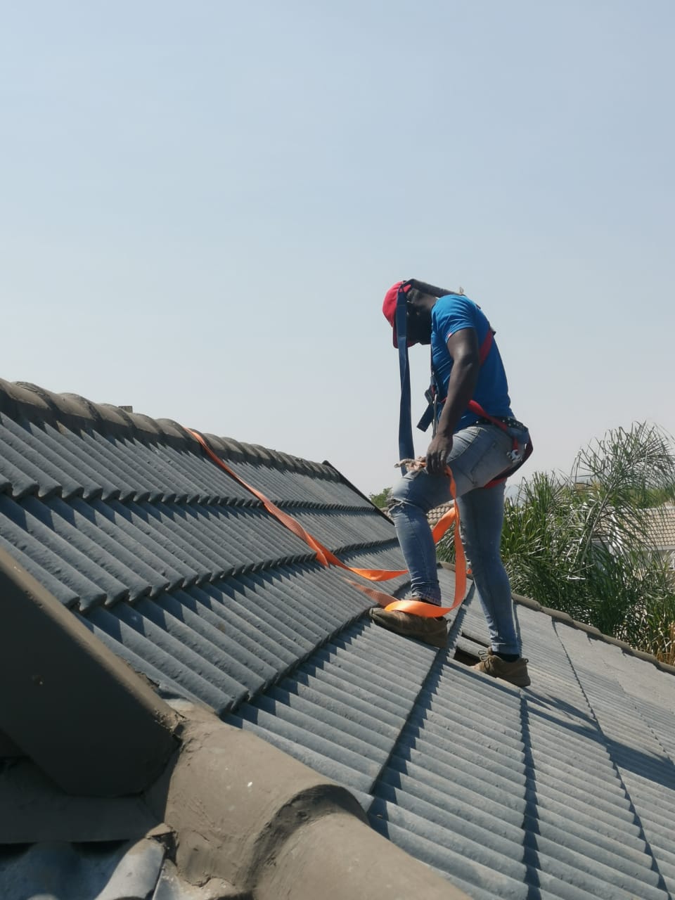 worker on roof with harness installing solar panel